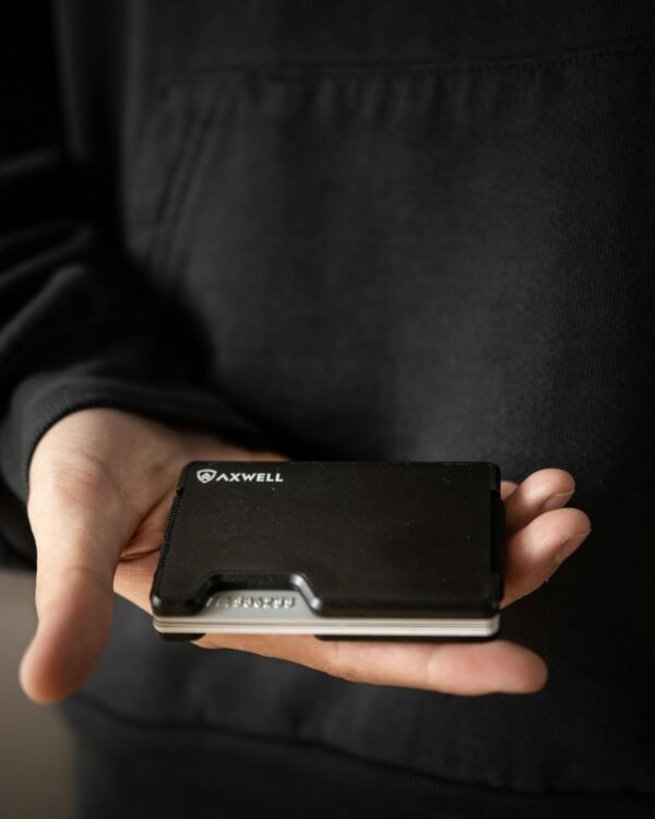 A detailed view of a hand presenting a sleek, black Axwell wallet against a dark background.